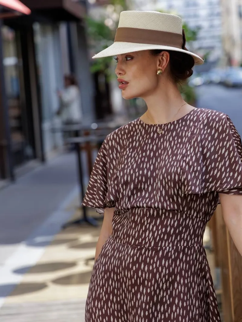 Profile view of the dash-print flutter-sleeve dress and straw boater on a Paris street