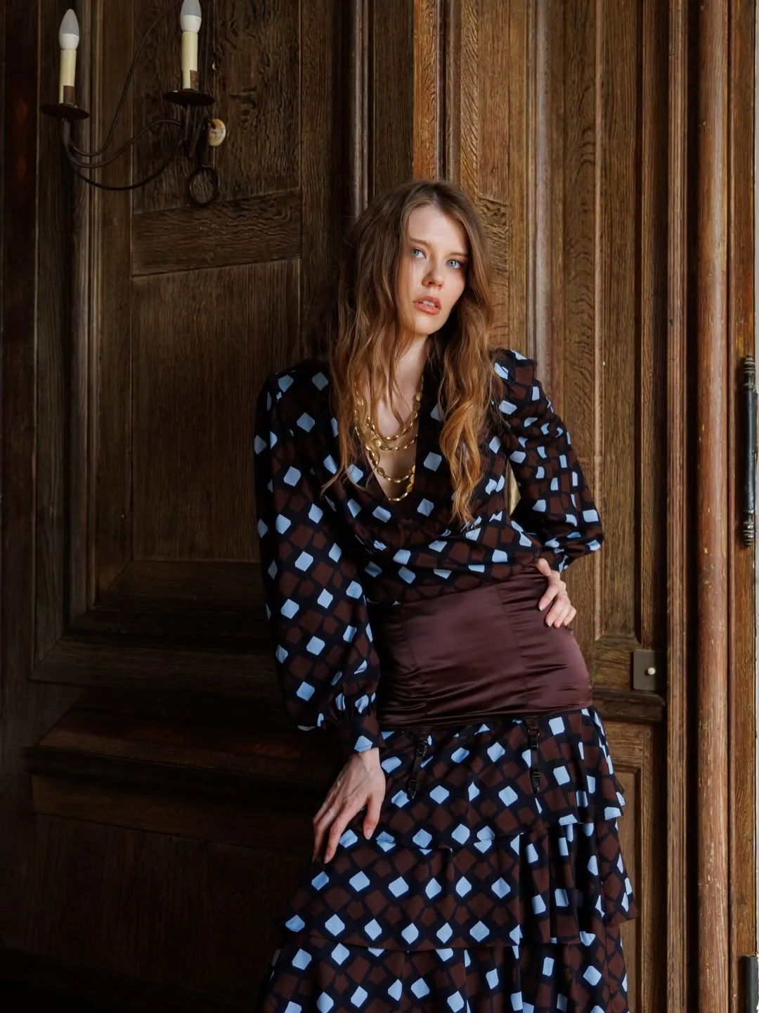 Model with a hand on her hip against an oak door, showing the satin waist cincher over the tiered diamond-print skirt