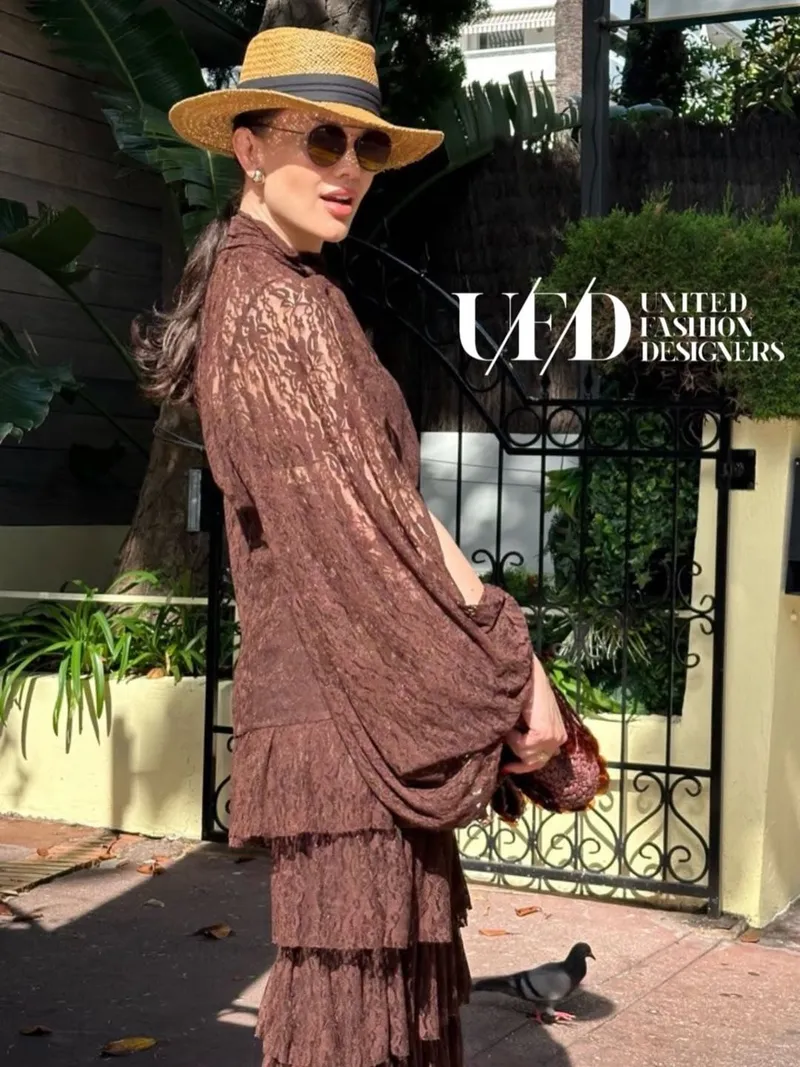 Model in a straw fedora and chocolate lace cape blouse beside a wrought-iron gate