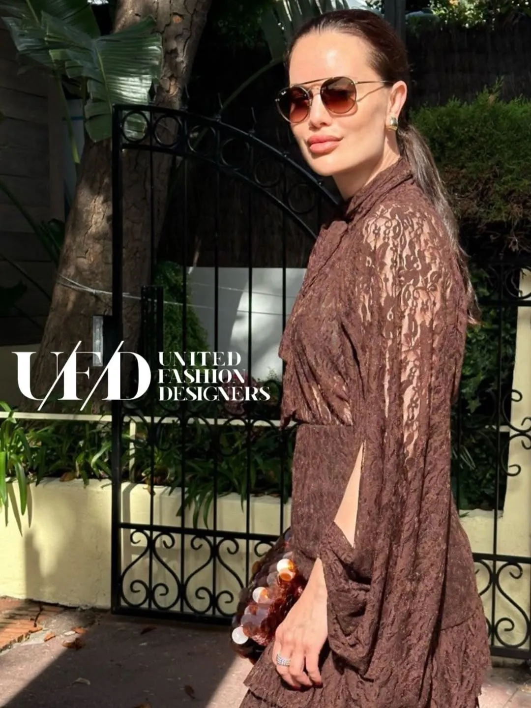 Close portrait in aviator sunglasses wearing the chocolate lace blouse, holding a paillette sequin bag