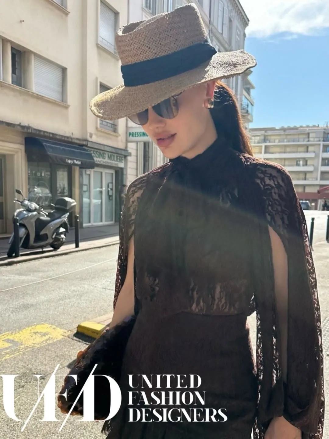Street portrait in a wide straw hat and chocolate lace cape on a sunny avenue
