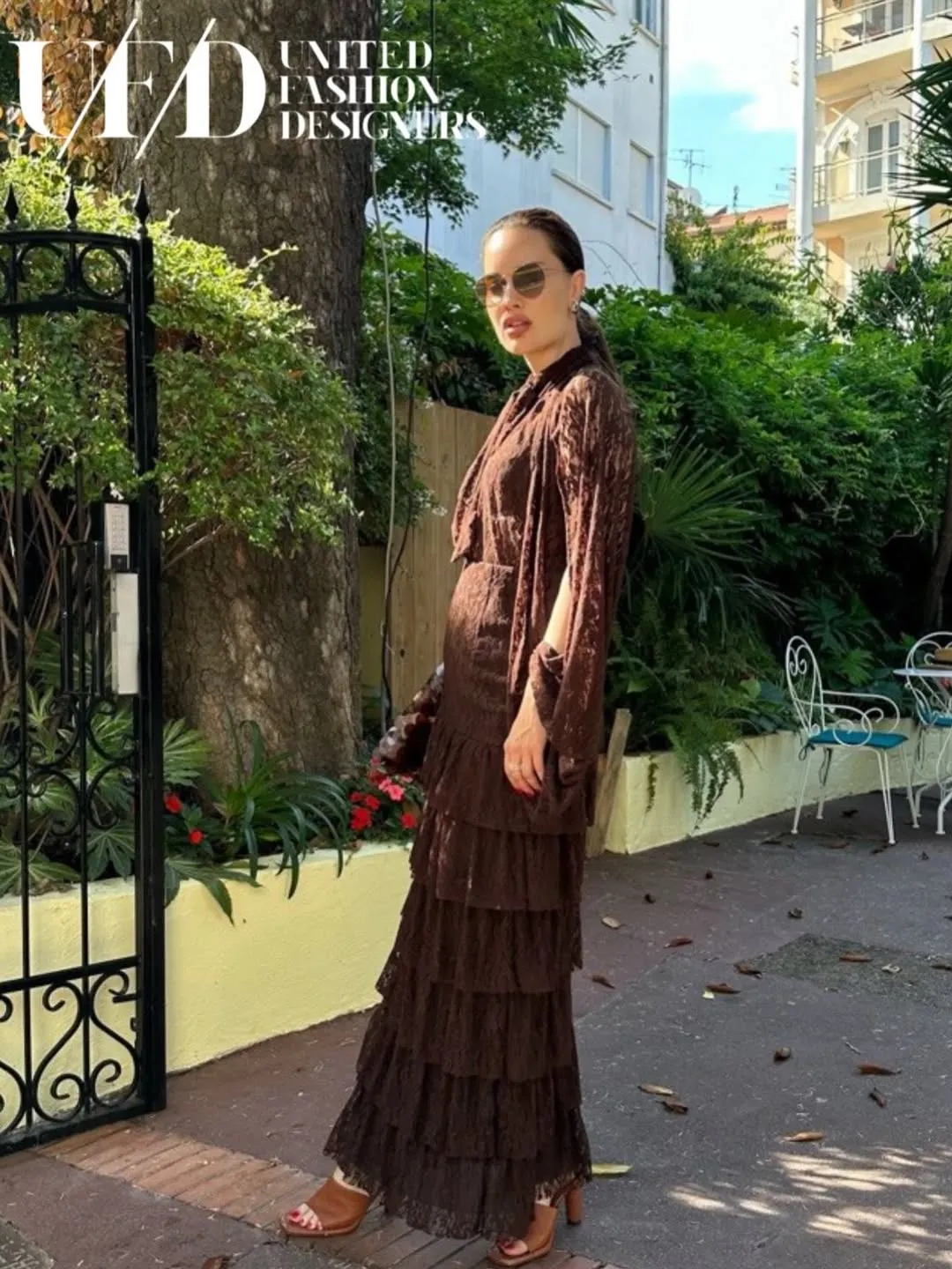 Full-length chocolate lace ensemble with tiered maxi skirt and tan heeled sandals in a garden courtyard