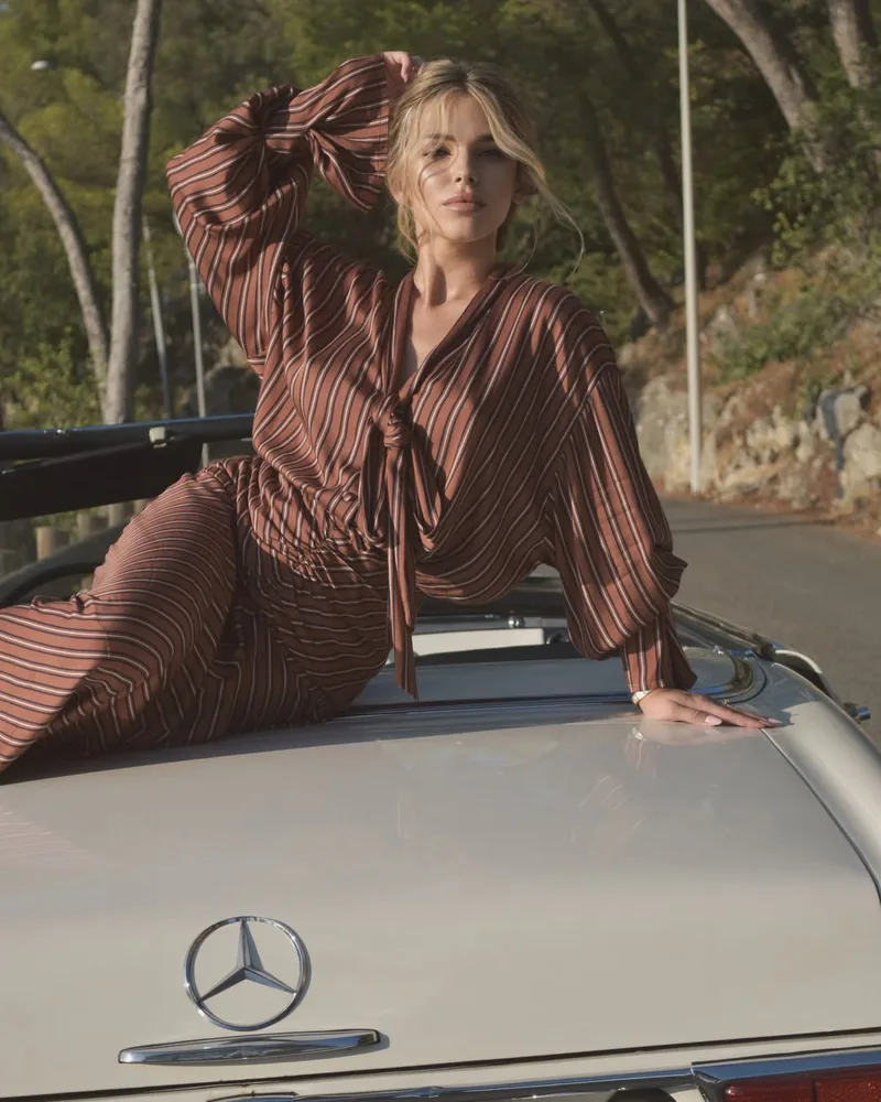 Model reclining across the cream boot of the convertible in the rust striped blouse and skirt