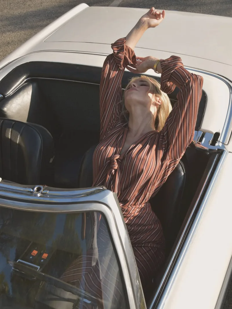 View from above of the model stretching in the driver’s seat, arms raised in the full striped sleeves