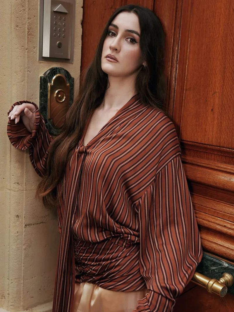 Close view of the oversized rust striped blouse with ruching at the hip, beside a brass door plate