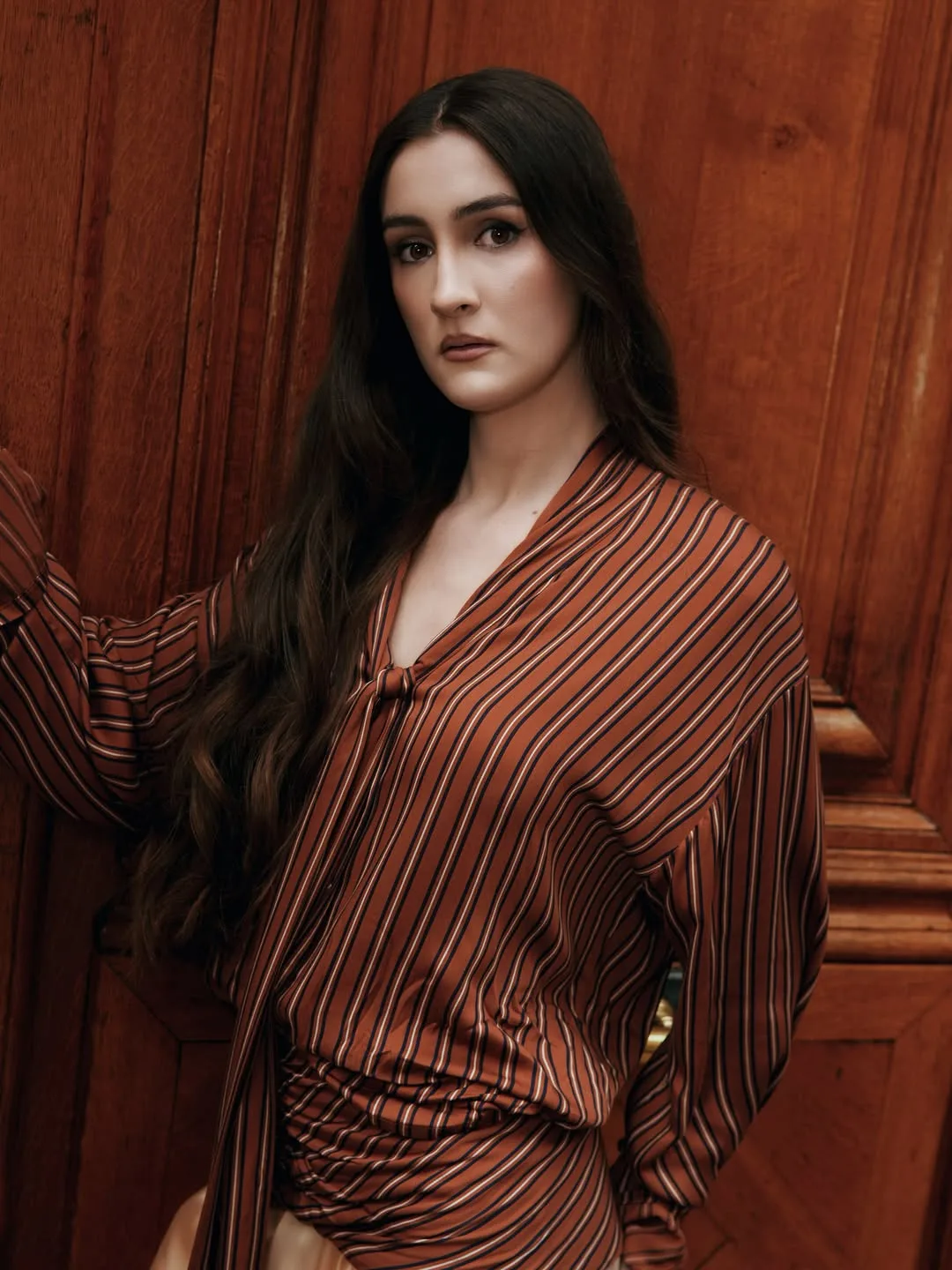 Portrait in the rust striped tie-neck blouse with dropped shoulders against a polished wooden door