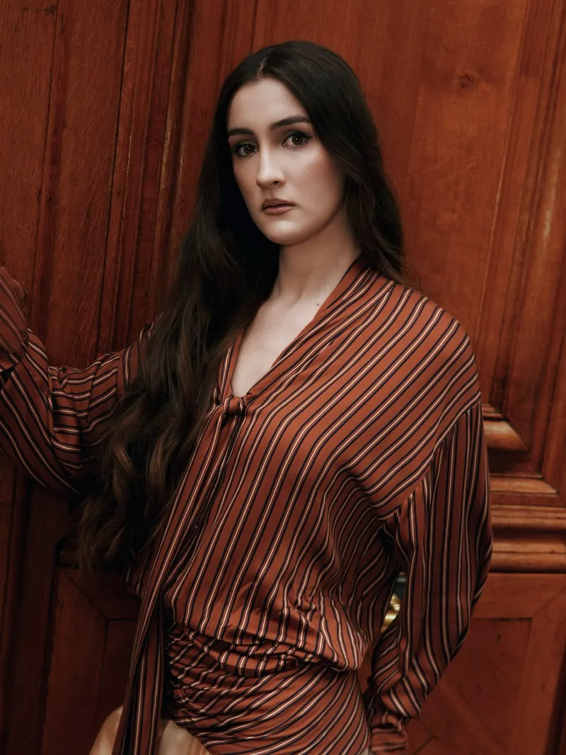 Portrait in the rust striped tie-neck blouse with dropped shoulders against a polished wooden door