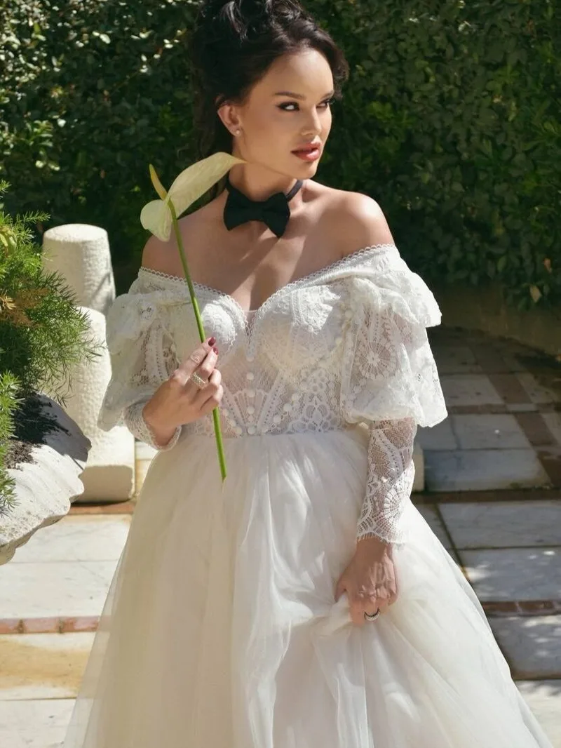 Model glancing over her shoulder, lace sleeves and calla lily catching the sun