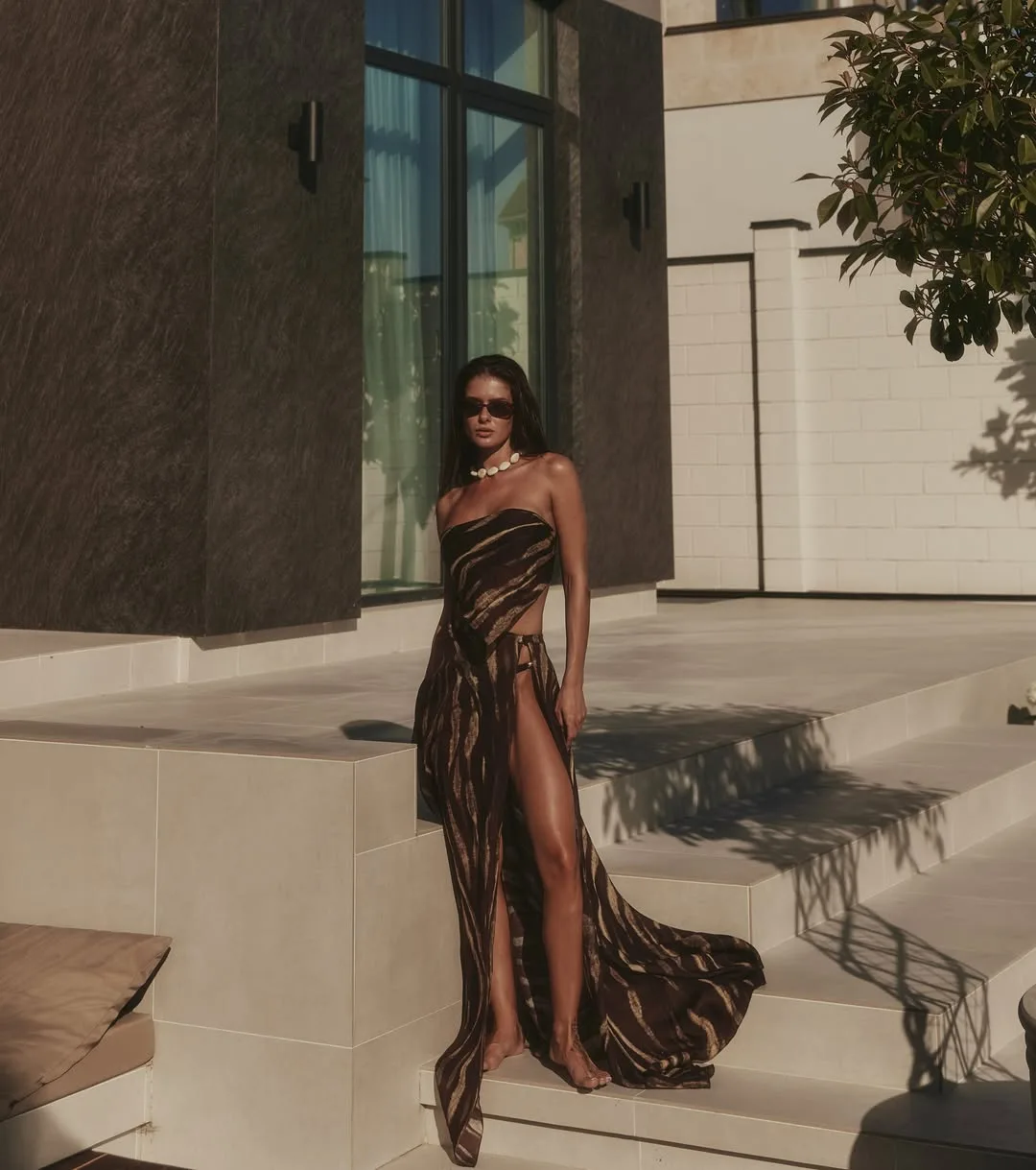 Model standing on pale stone steps in the striped bandeau and wrap maxi skirt with a sweeping train